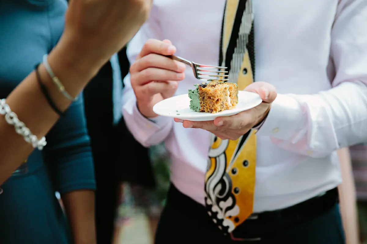 Guest in a patterned tie holding a plate with a slice of cake and a fork