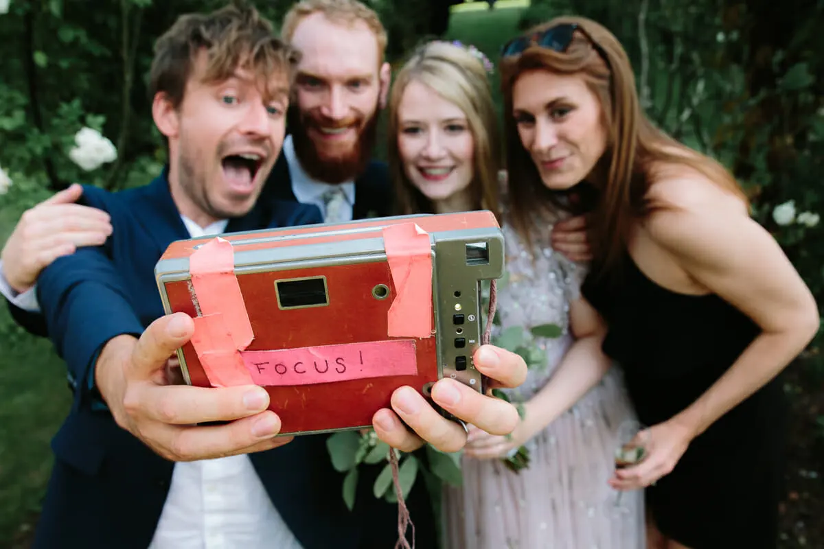 Four guests including the bride and groom posing for a selfie with a retro instant camera