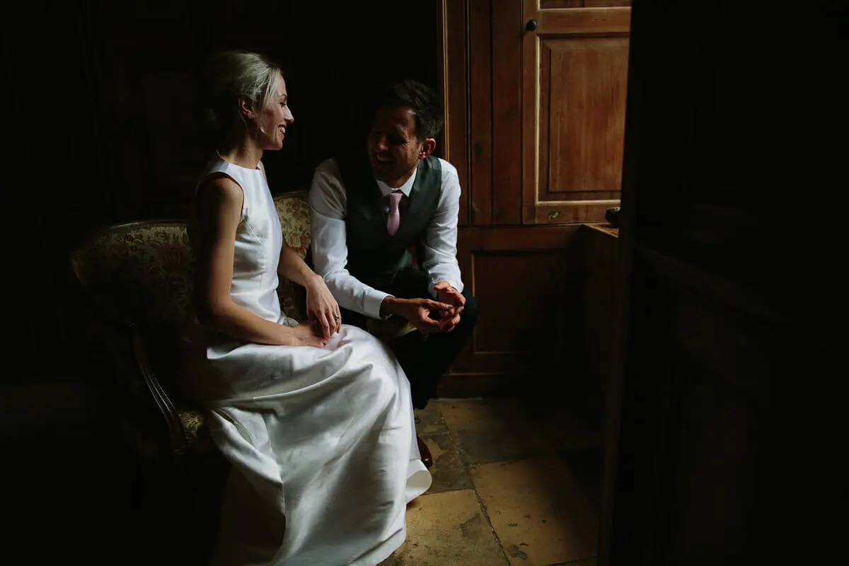 Bride and groom sitting together and laughing in a dim wood-panelled room
