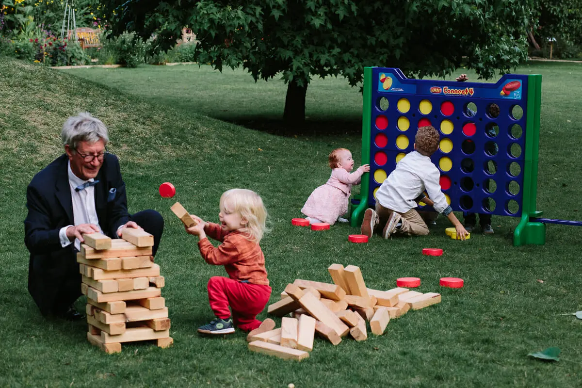 Older guest building a giant Jenga tower with a toddler as children play giant Connect 4