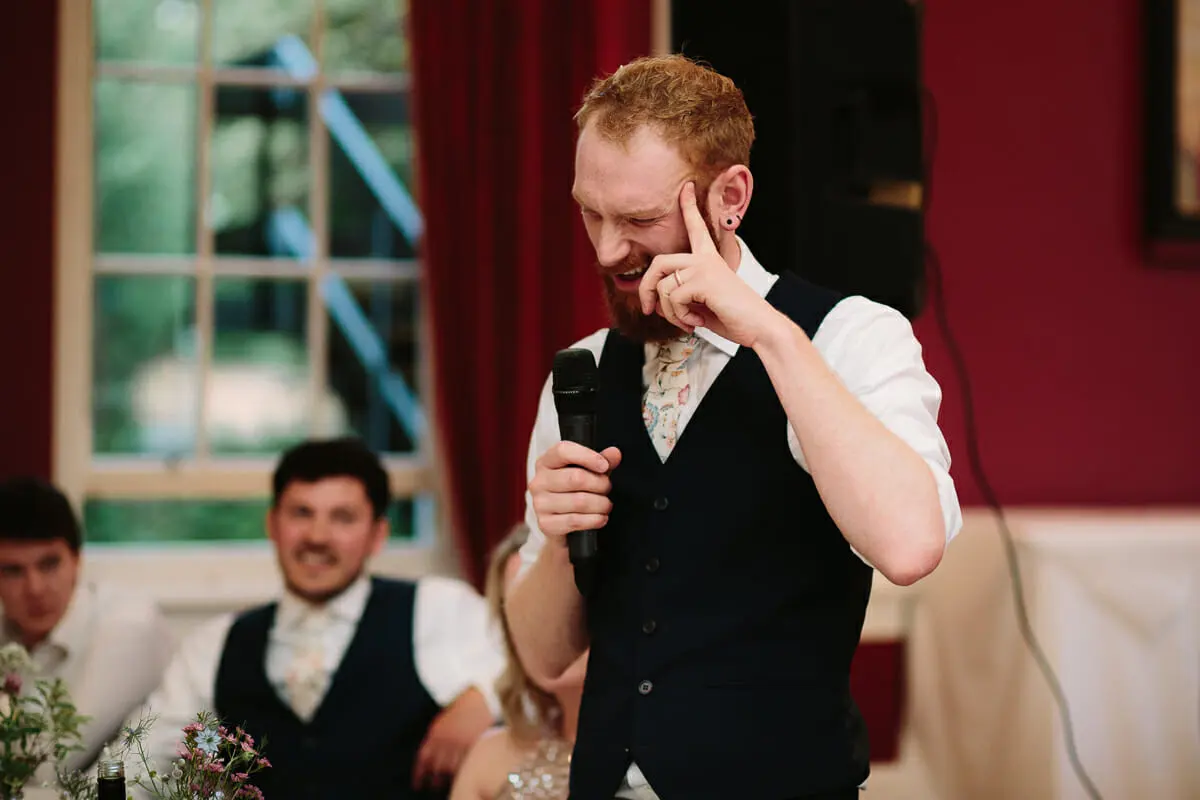 Groom laughing and tapping his head as he gives his speech into a microphone