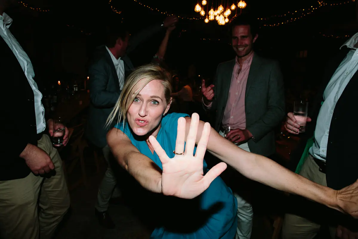 Guest in a teal dress throwing out a hand towards the camera as she dances under festoon lights