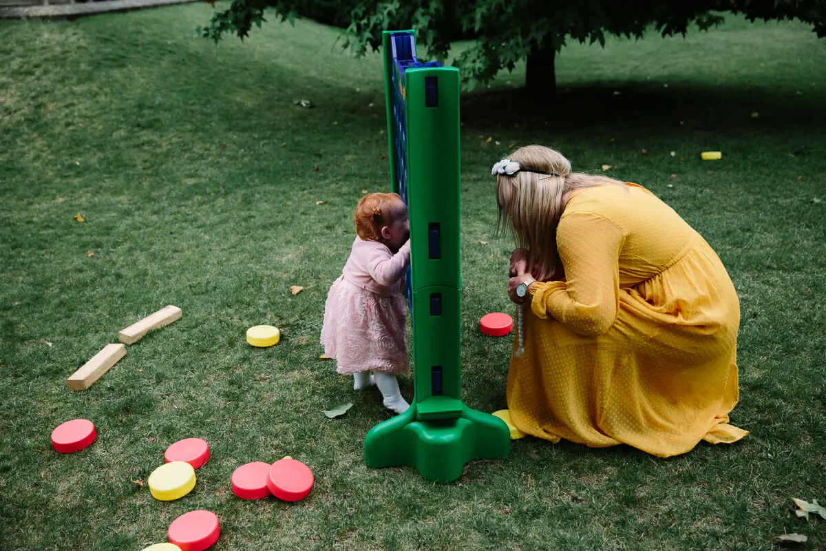 Toddler and a woman in a yellow dress playing giant four in a row on a lawn