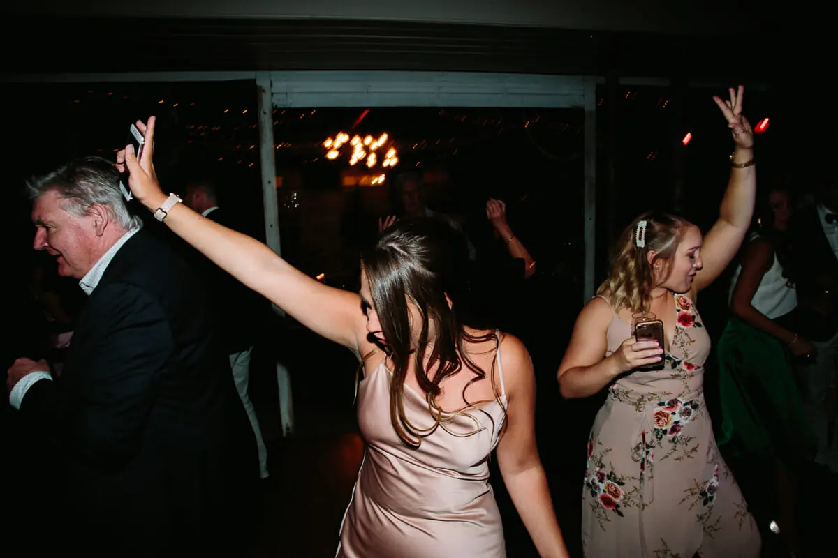 Guests dancing with arms raised on a dark dance floor under warm lights
