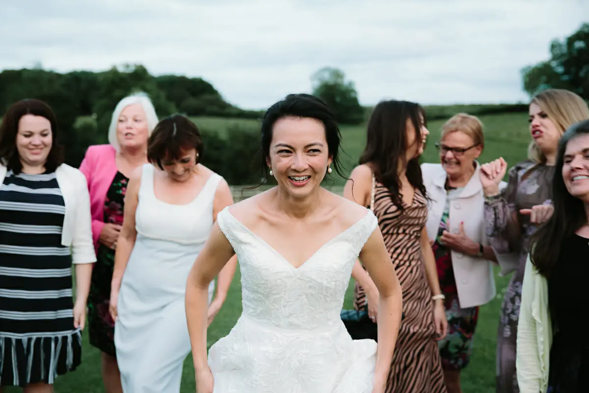 Smiling bride striding across a field ahead of a group of female guests