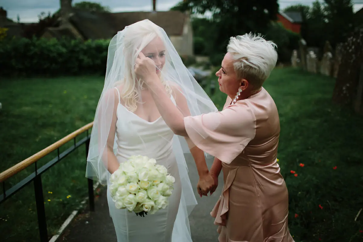 Woman in a pink satin dress adjusting the bride's veil on a churchyard path