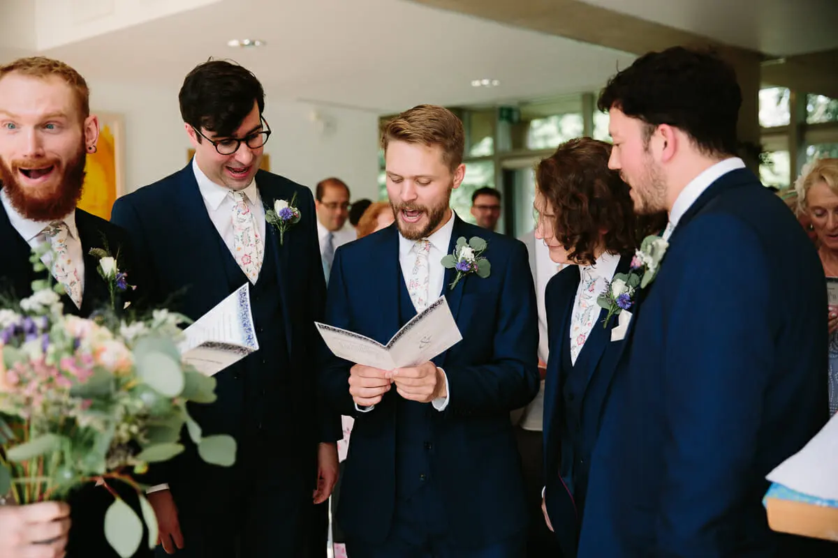 Groomsmen in navy suits singing from their orders of service