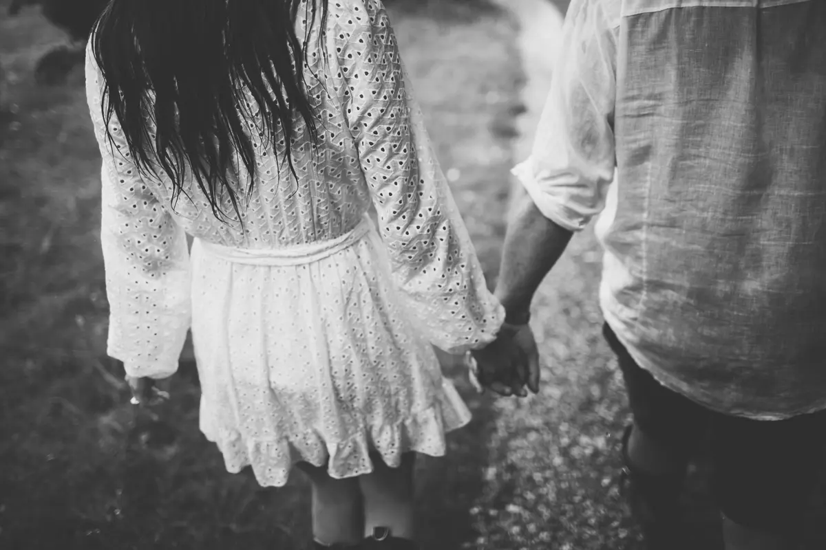 Black and white view from behind of a couple holding hands as they walk along a path