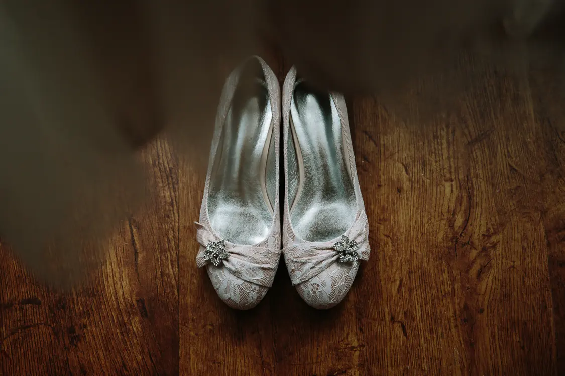 Pair of lace bridal shoes with jewelled brooches on a wooden floor