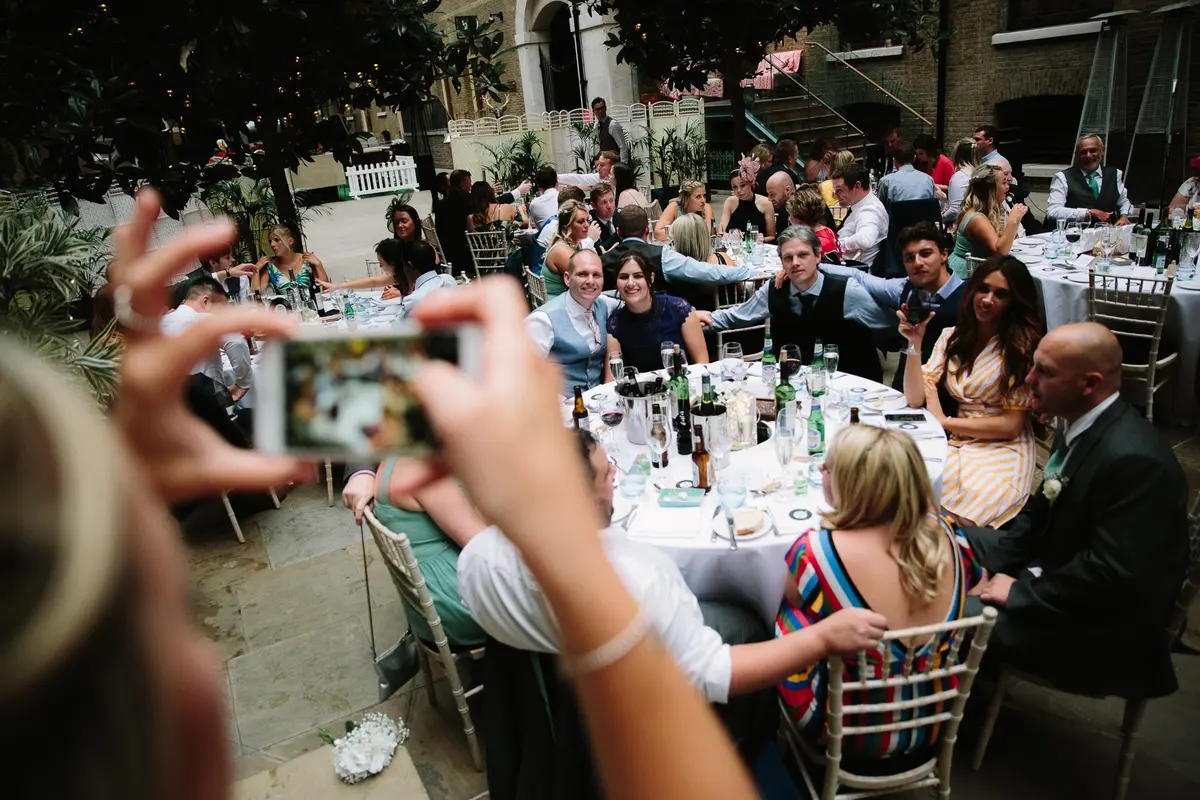 Guest taking a phone photo of a table of guests at an outdoor courtyard reception