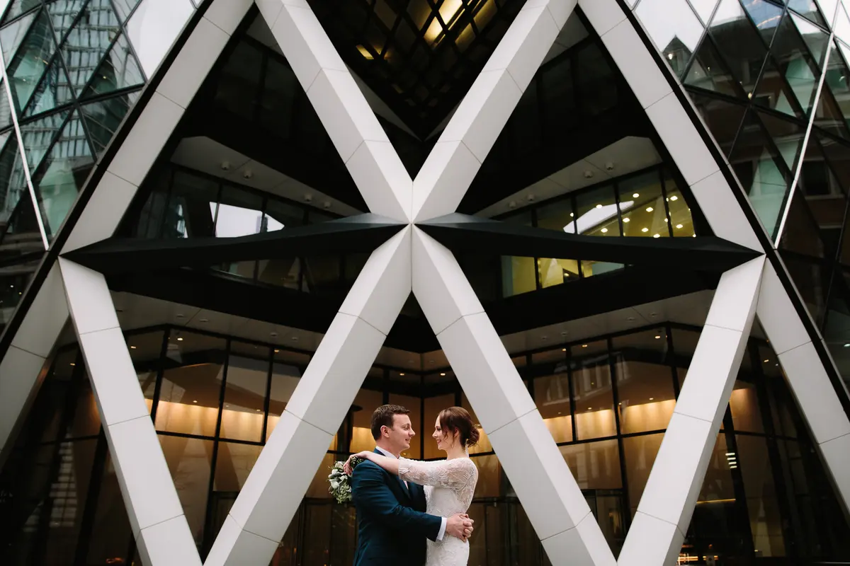 Bride and groom embracing beneath the criss-cross steel frame of the Gherkin in London
