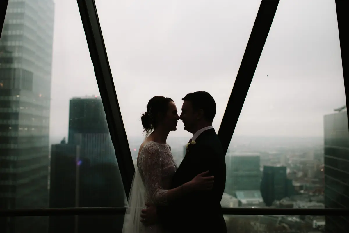Bride and groom silhouetted nose to nose at an angled window high above the City of London