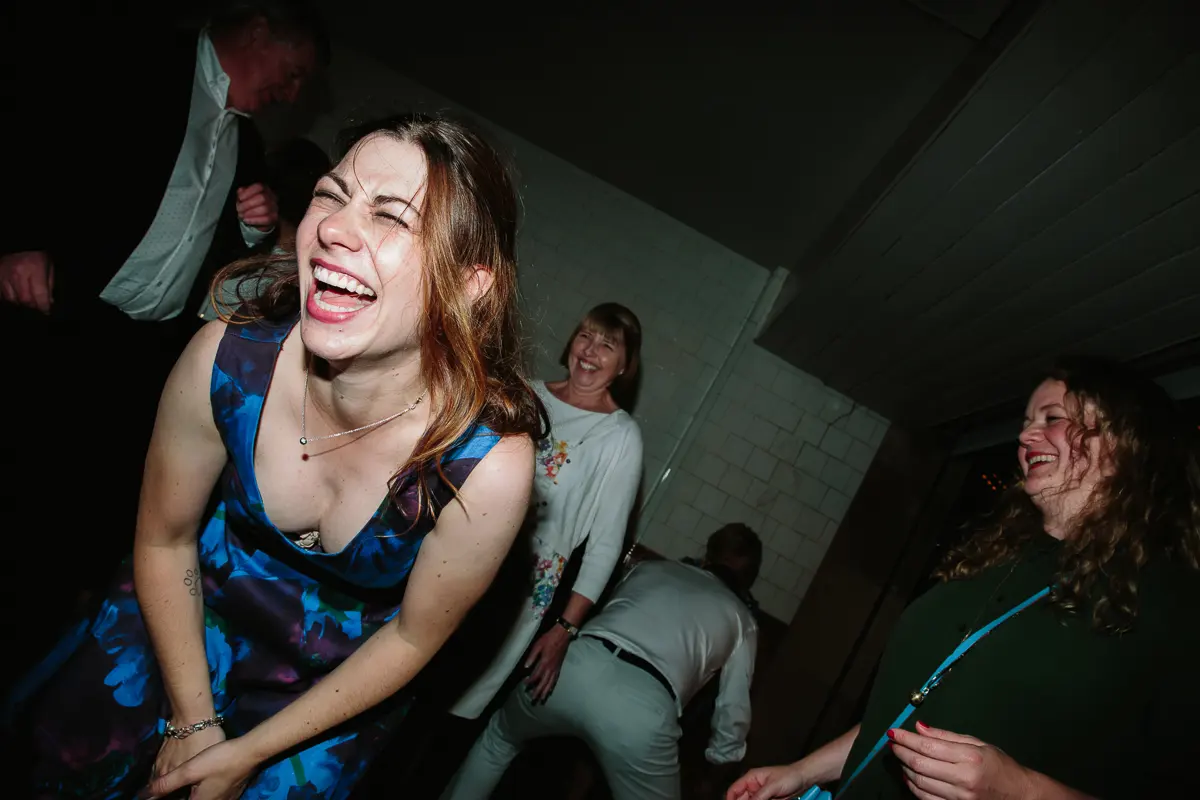 Guest in a blue floral dress doubled over laughing on the dance floor
