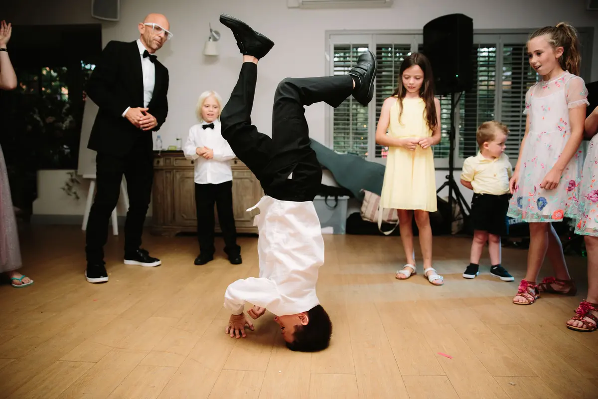 Boy in a white shirt doing a headstand on the dance floor as other children watch