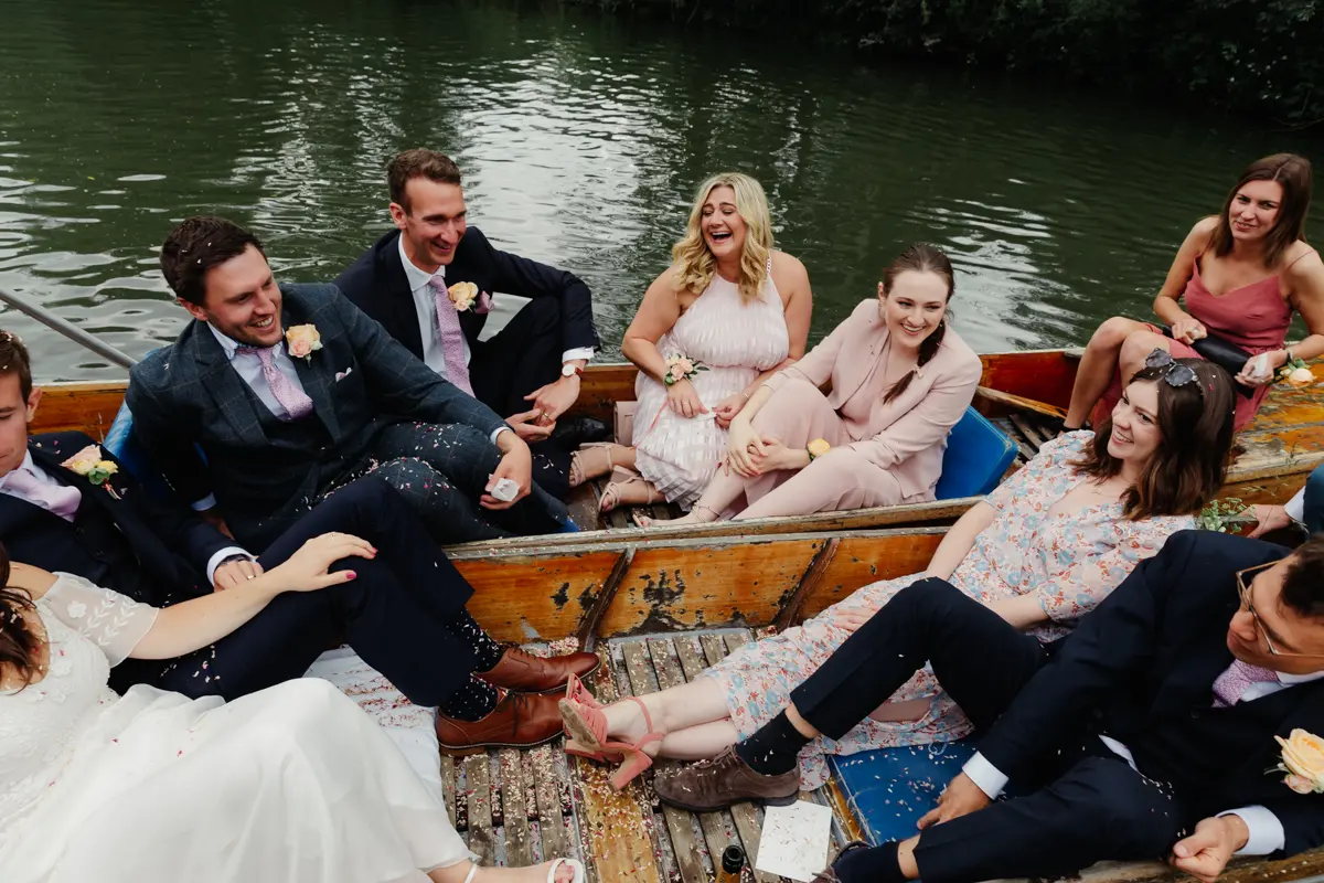 Bride, groom and friends laughing together in a punt on the river, covered in confetti