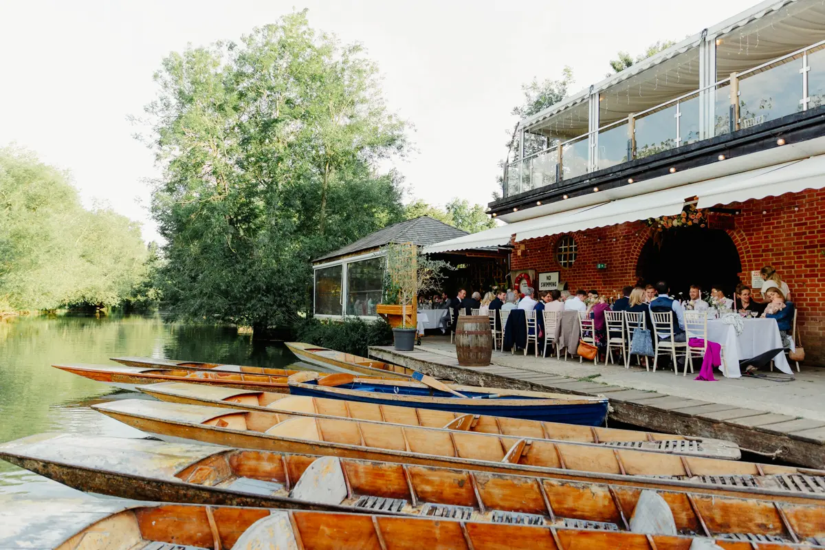 Wedding guests dining on the terrace at Cherwell Boathouse, with a row of punts moored in front