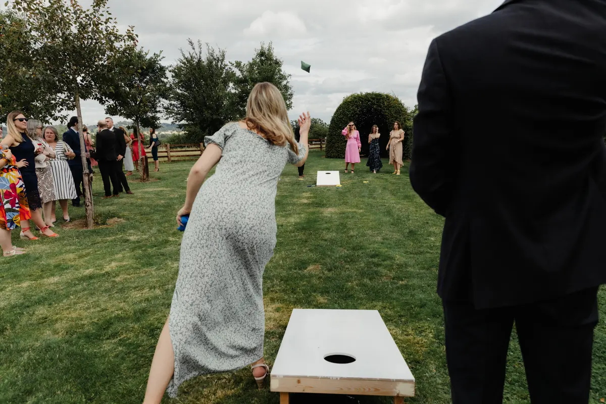 Guest throwing a beanbag at a cornhole board as others watch on the lawn at Primrose Hill Farm