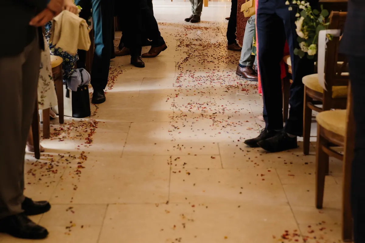 Petal confetti scattered along the aisle between guests' feet after the ceremony at Caswell House