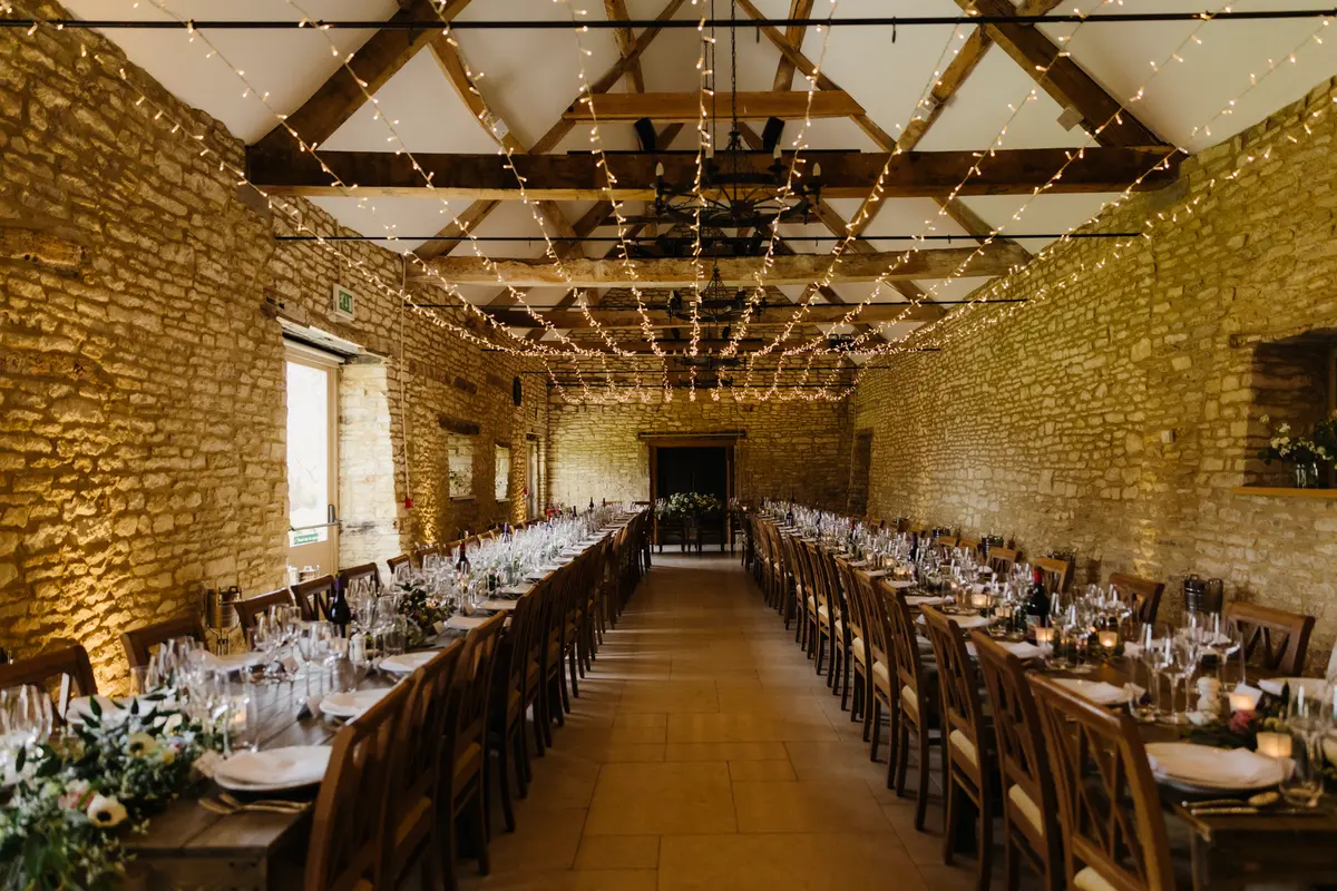 Long tables beneath fairy lights and oak beams in the stone barn at Caswell House