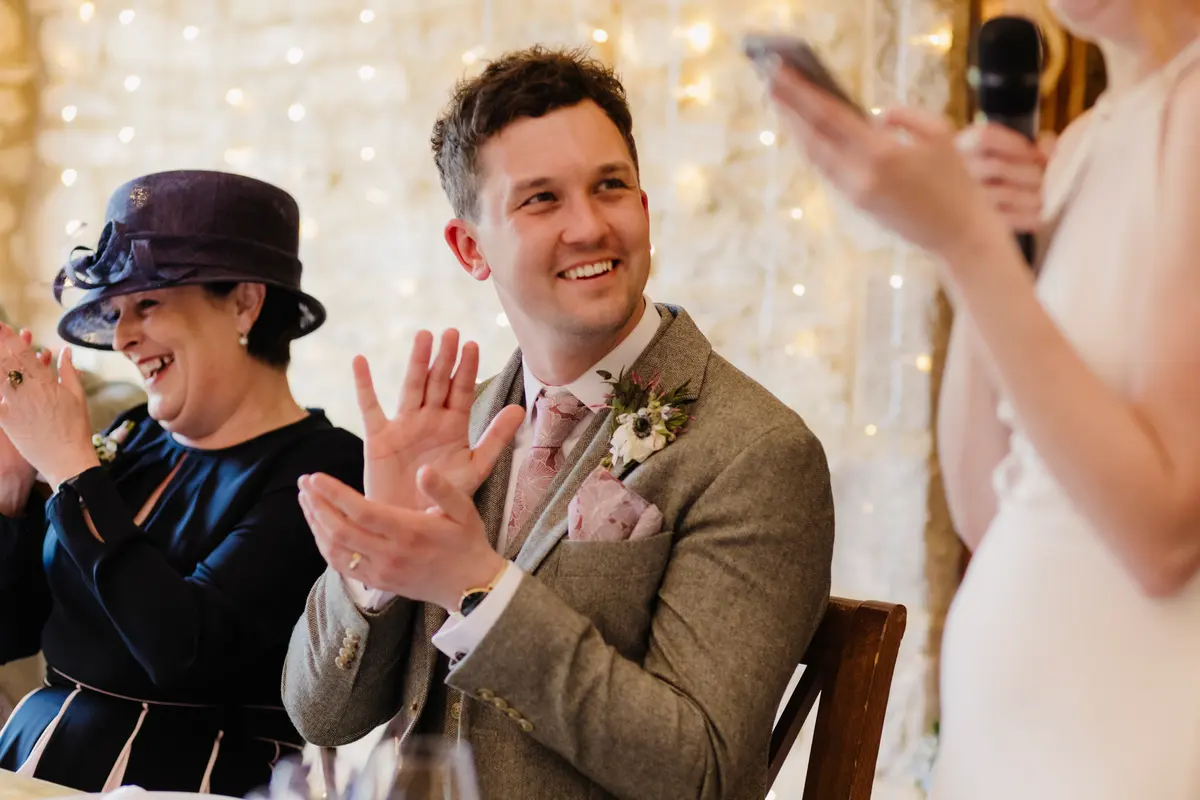 Groom and a guest in a hat clapping during the bride's speech at Caswell House