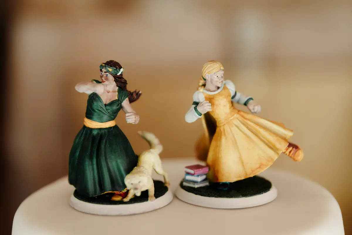 Hand-painted cake toppers of two women in green and yellow gowns, one with a small dog