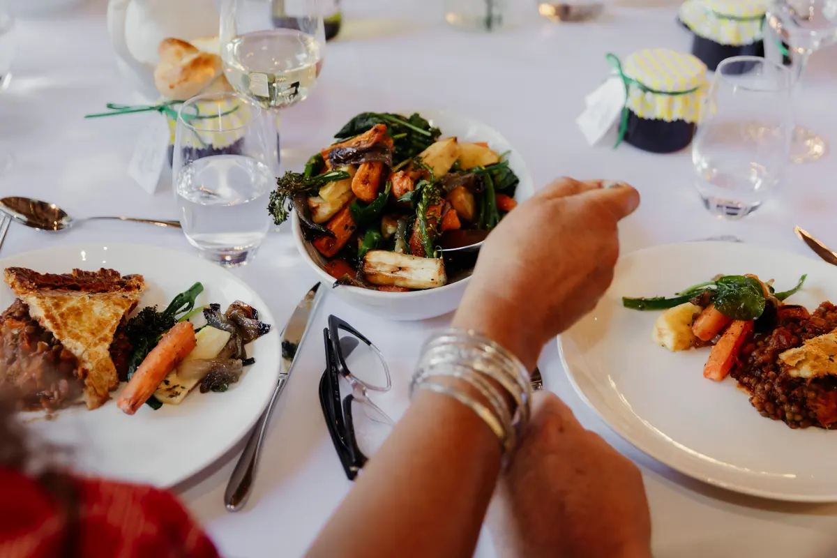 Guest reaching for a bowl of roast vegetables at a family-style wedding meal at Lains Barn
