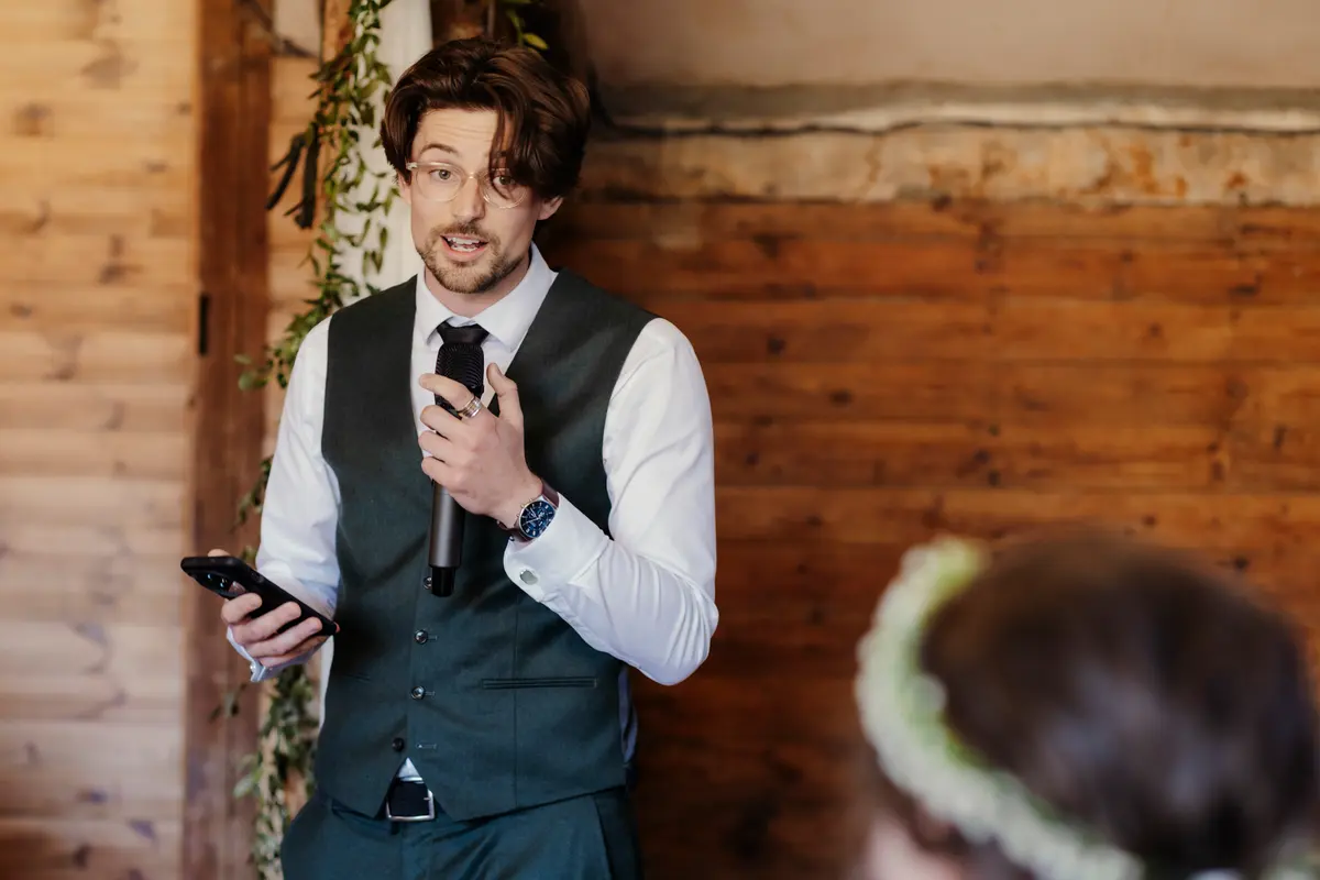 Guest in glasses and a waistcoat giving a speech with a microphone and phone at Lains Barn