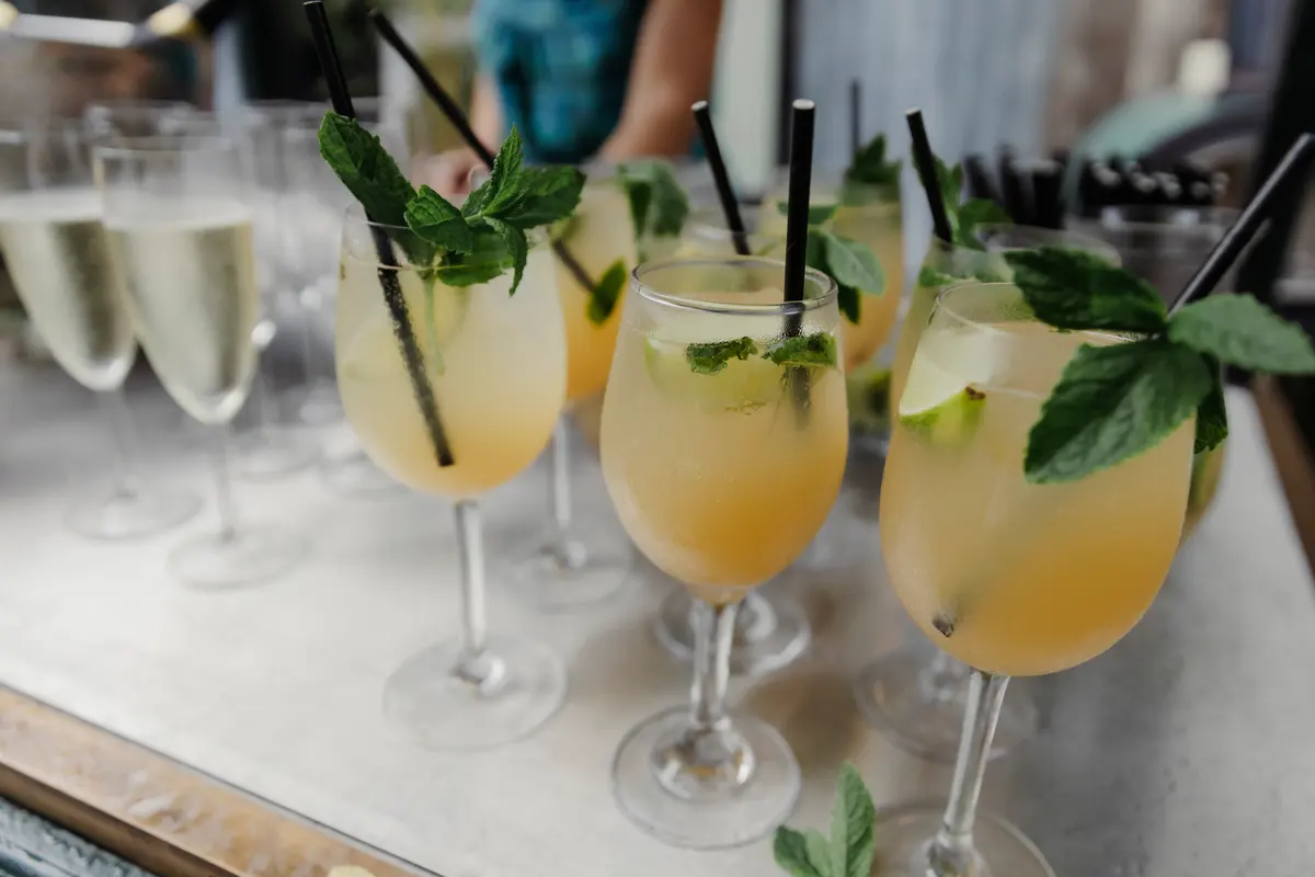 Glasses of cocktails with mint, lime and black straws lined up beside flutes of fizz
