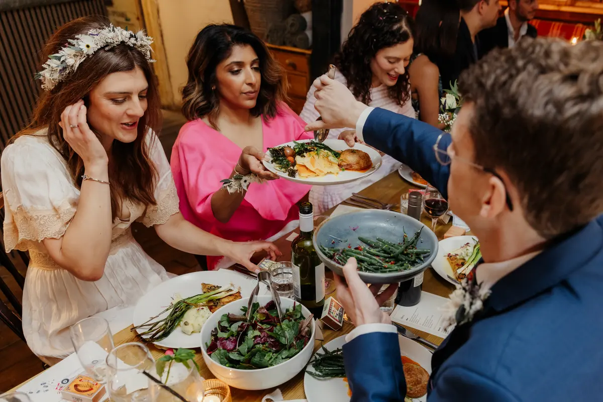 Bride and guests sharing plates of food at a long table during the wedding meal