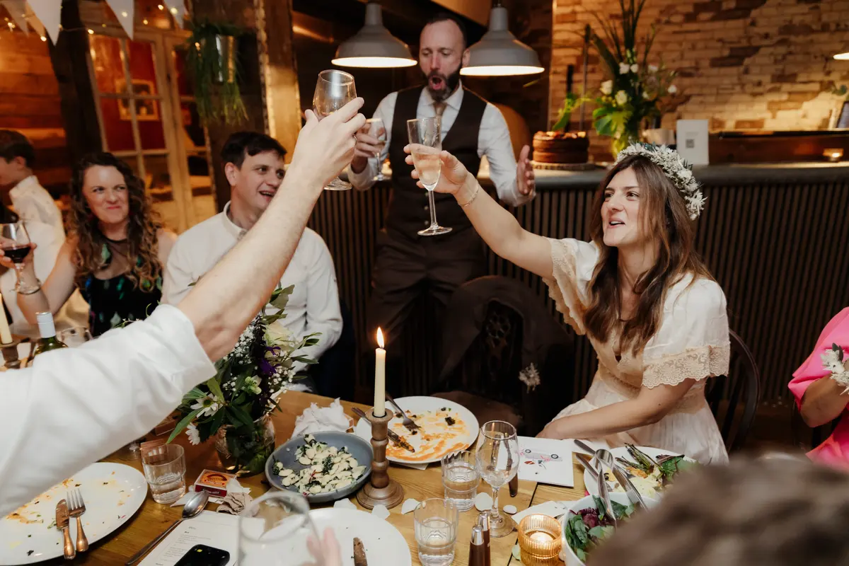 Bride raising her glass in a toast with guests around the dinner table