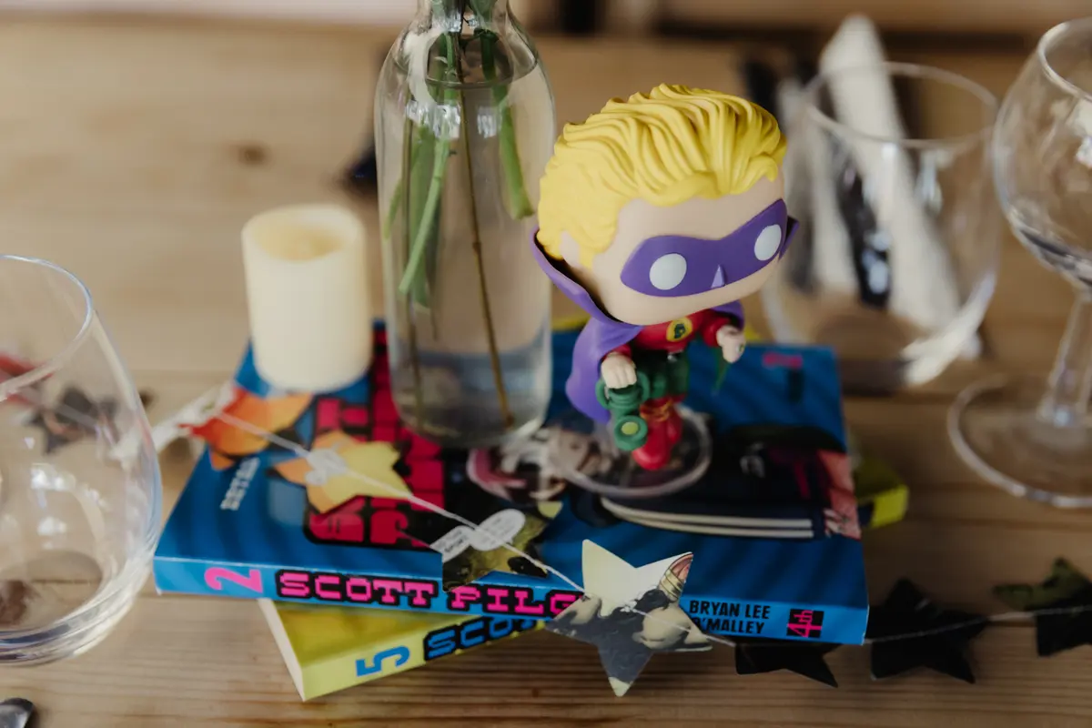 Toy superhero figure on Scott Pilgrim comics as a table centrepiece with a bottle vase and candle