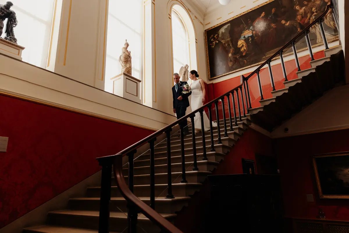 Bride and her father walking down the grand red-walled staircase at the Ashmolean Museum