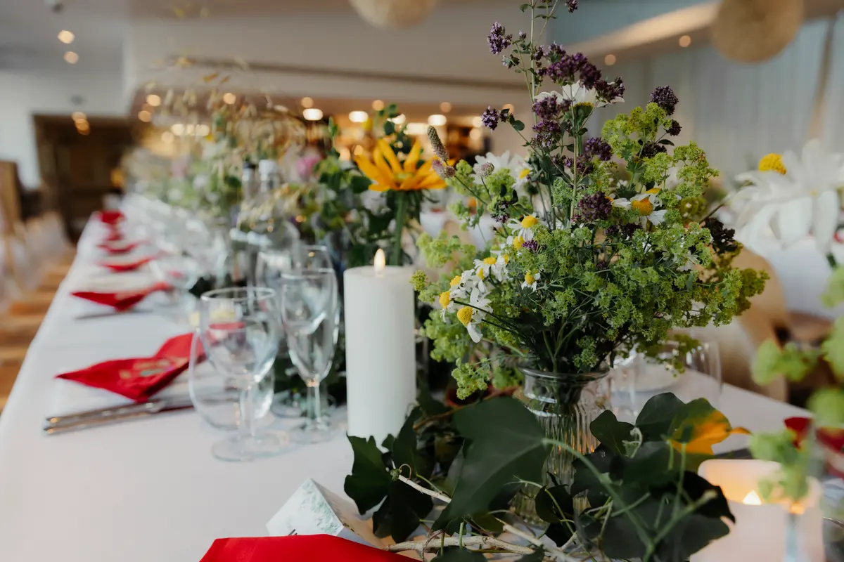 Wild flowers, pillar candles and red napkins along a long white reception table