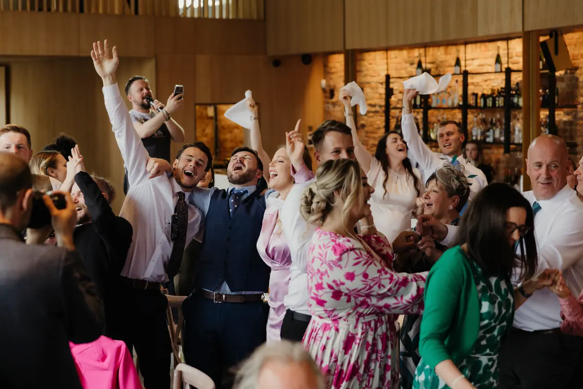 Guests cheering and waving napkins in the air as a singer performs during the wedding breakfast