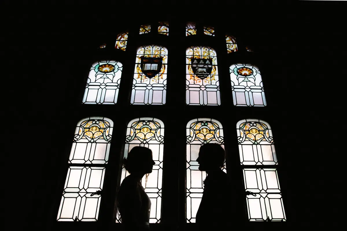 Bride and groom silhouetted face to face against a tall stained glass window